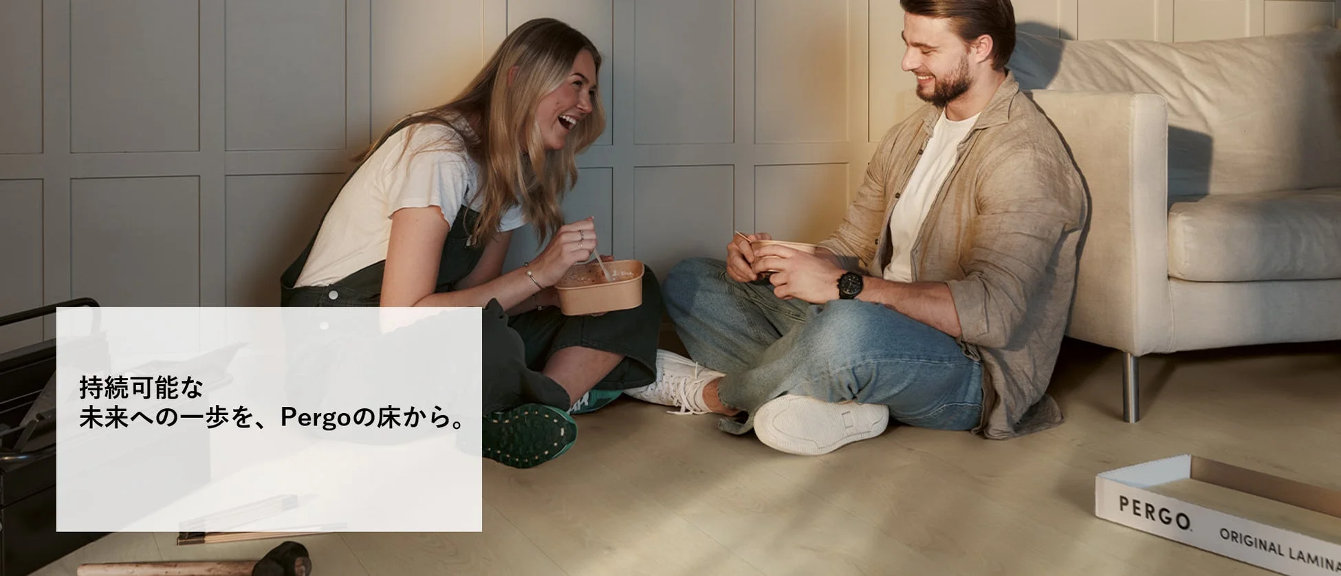 新しいフローリングの上で笑顔で食事をするカップルの画像です。Pergoの床材が持続可能な未来への一歩であることを示唆するテキストが添えられています。