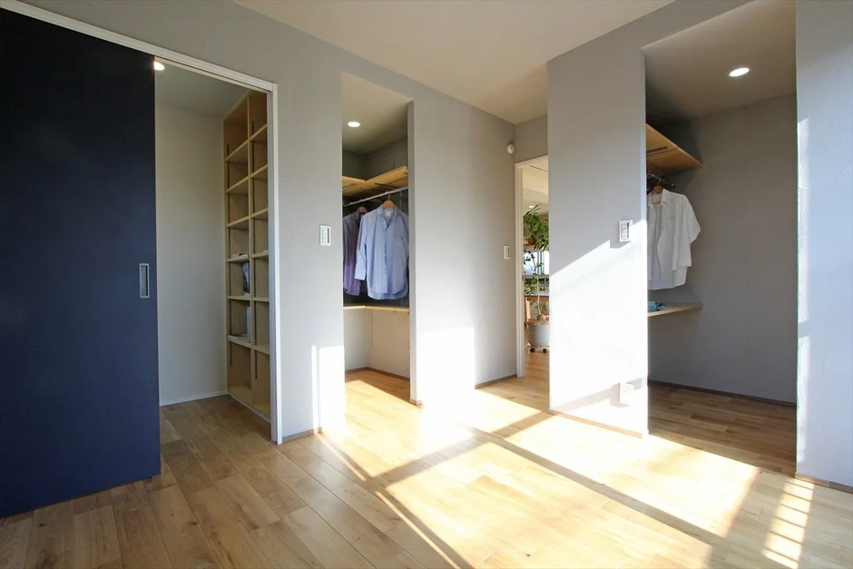 明るい日差しが差し込むモダンな住宅の廊下です。複数の収納スペースがあり、木製のフローリングとグレーの壁が特徴的で、すっきりとした印象を与えます。