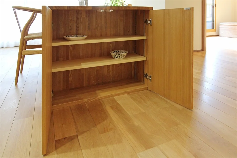 明るい木目のフローリングの部屋に設置された木製キャビネットが開いており、棚には小さな器が置かれています。ナチュラルで清潔感のある空間です。
