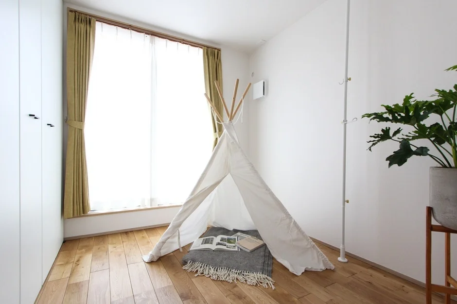明るい日差しが差し込む部屋に、白いティピーテントが設置された居心地の良い空間。木製フローリングと白い壁が清潔感を演出し、観葉植物がアクセントになっています。