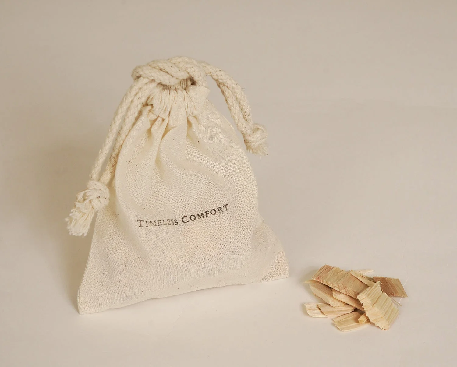 ベージュの布製巾着袋と木材チップが写っています。巾着袋には「TIMELESS COMFORT」と書かれており、素朴で穏やかな雰囲気が漂う画像です。