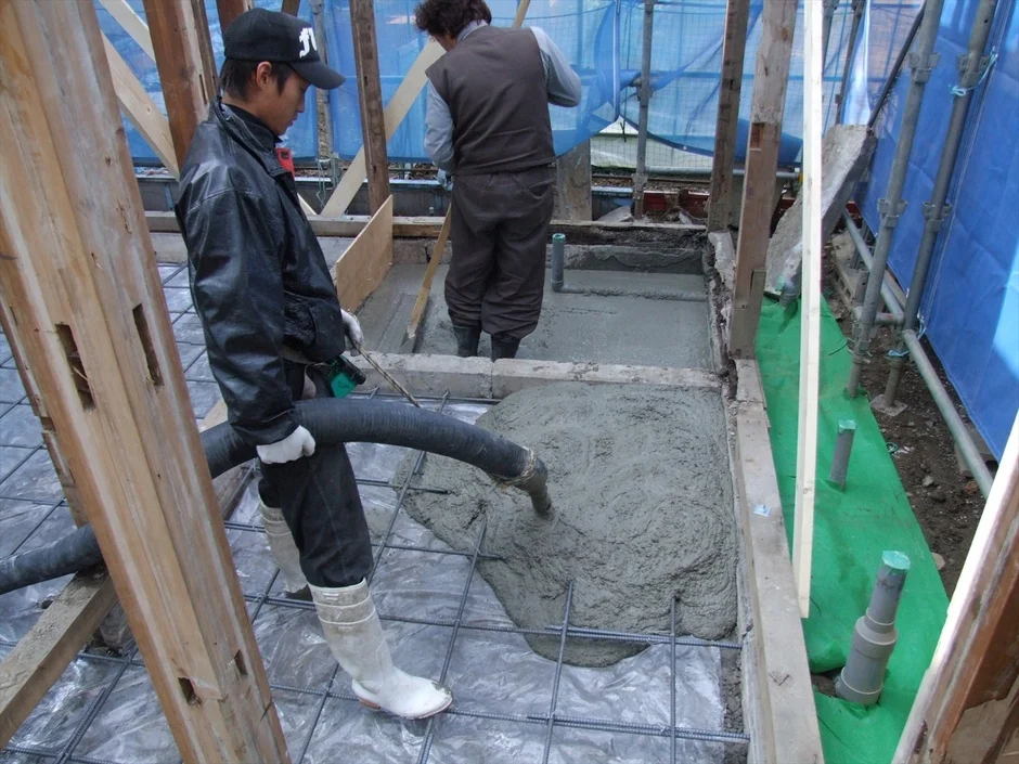 コンクリートポンプで基礎に生コンクリートを打設する作業員