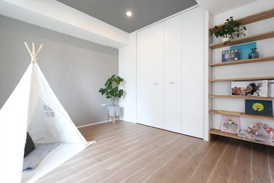 白いティピーテントが置かれた明るい子供部屋のインテリア。白いクローゼットと木製の本棚があり、観葉植物がアクセントになっています。モダンでシンプルな空間です。