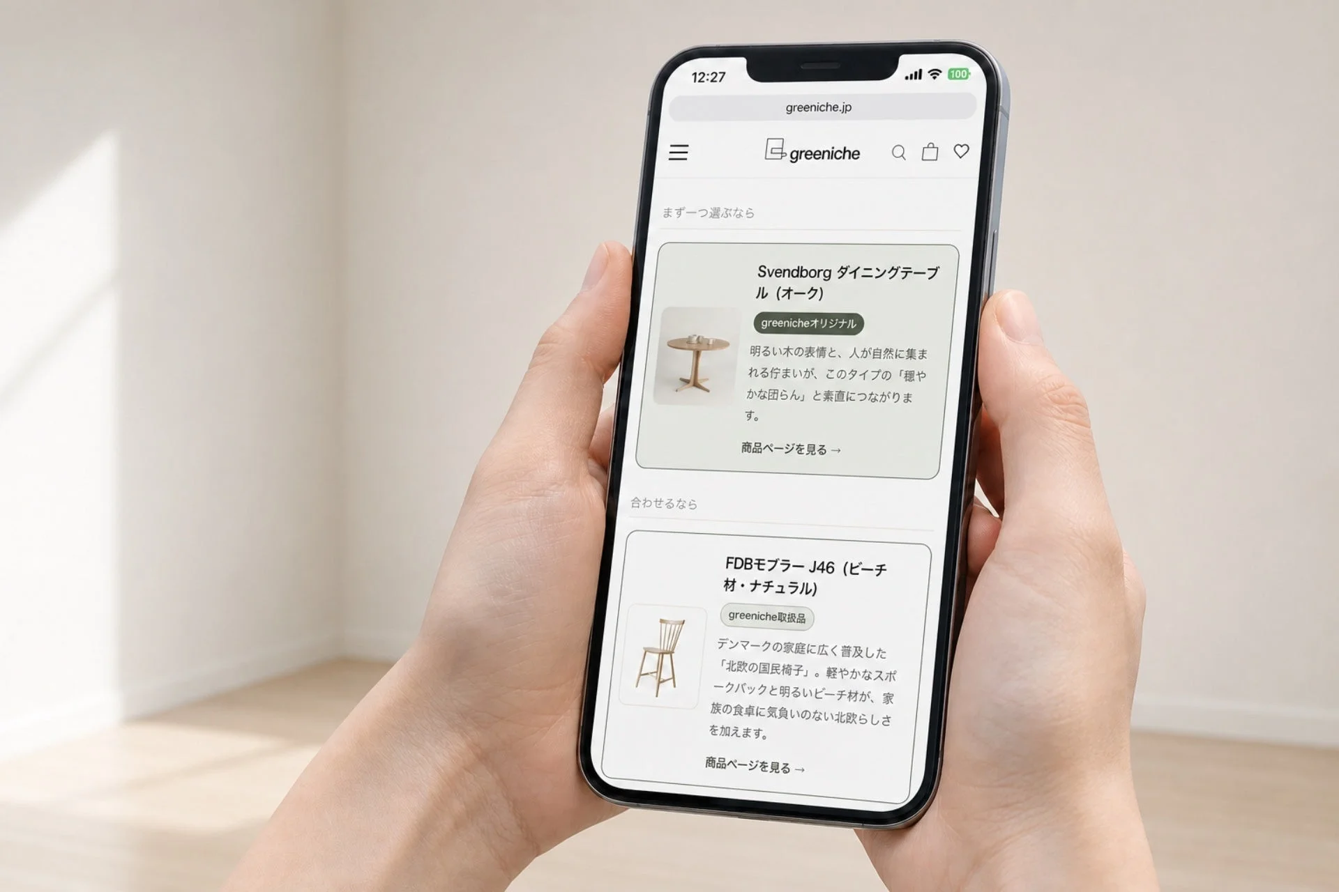 両手でスマートフォンを持ち、北欧家具のオンラインストア「greeniche」のウェブサイトを閲覧している様子。ダイニングテーブルと椅子の商品情報が表示されており、詳細な説明文も確認できます。