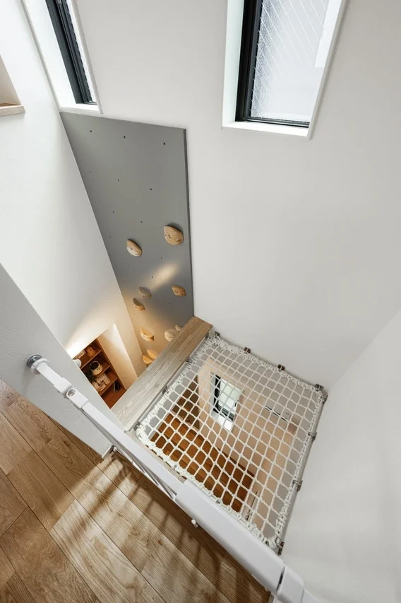モダンな住宅の吹き抜け空間に、ボルダリングウォールと遊び心のあるセーフティネットが設けられたインテリアデザイン