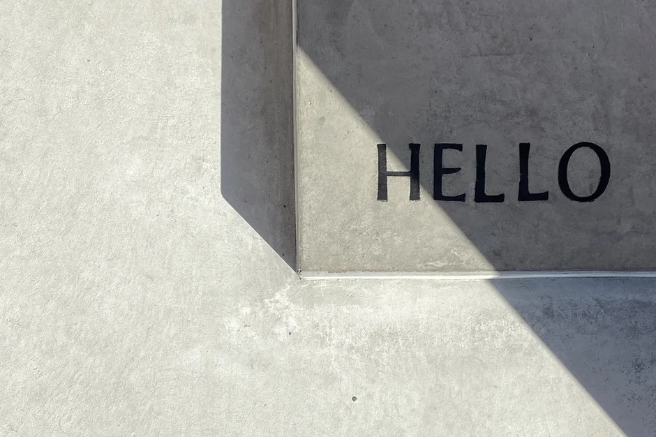 コンクリートの壁に「HELLO」という文字が刻まれ、強い日差しが影を落としている