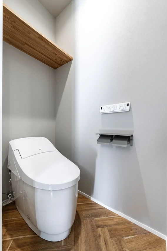 明るいグレーの壁とヘリンボーン柄の木目調フローリングが特徴の、モダンで清潔感のあるトイレ空間