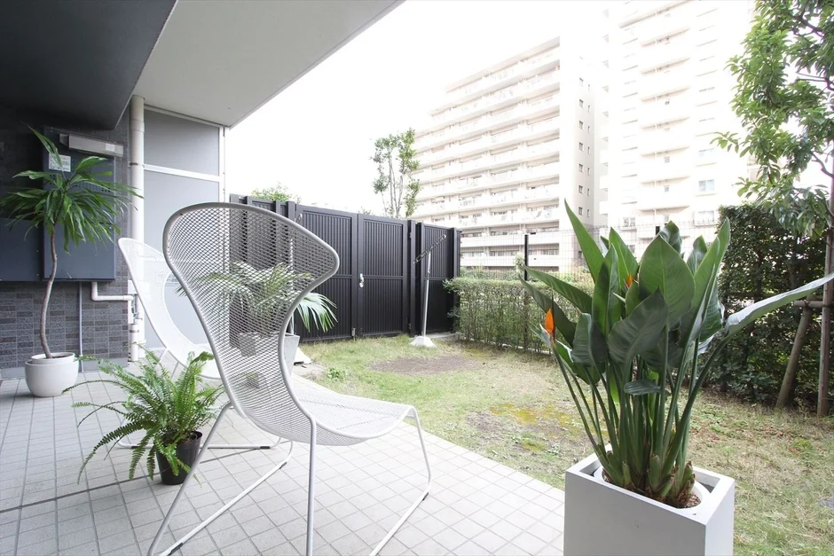 モダンな白いメッシュチェアと様々な観葉植物が配置されたテラスと庭の風景