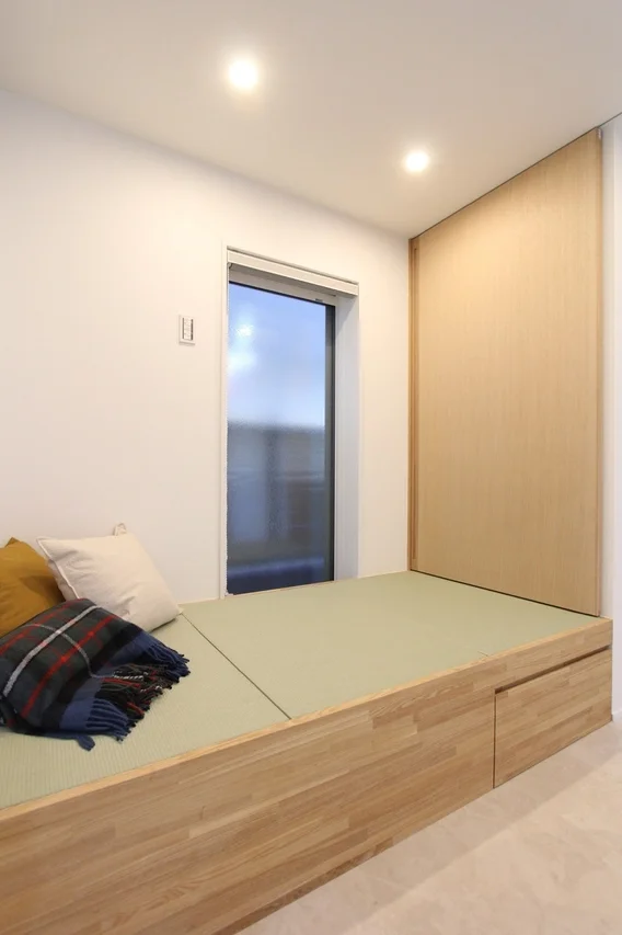 和モダンな雰囲気の部屋で、木製の小上がりに畳が敷かれ、クッションとブランケットが置かれている