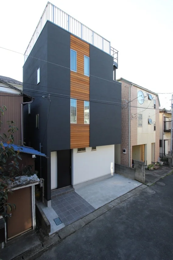 ダークグレーの外壁と木製パネルが特徴的な3階建ての現代的な住宅