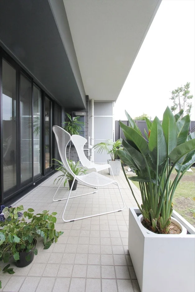 モダンな建物のバルコニーまたはテラスが写っており、白いメッシュチェアと複数の観葉植物が配置