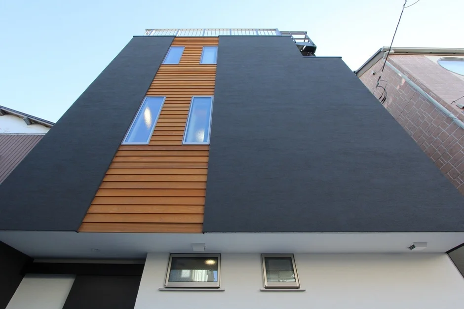 黒い壁と木目調のパネルが印象的な、現代的なデザインの建物の外観写真