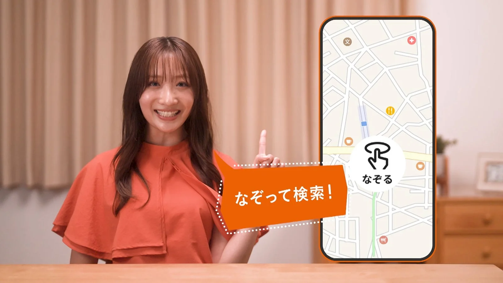 笑顔の女性が、スマートフォンに表示された地図アプリの「なぞって検索」機能を指し示しています
