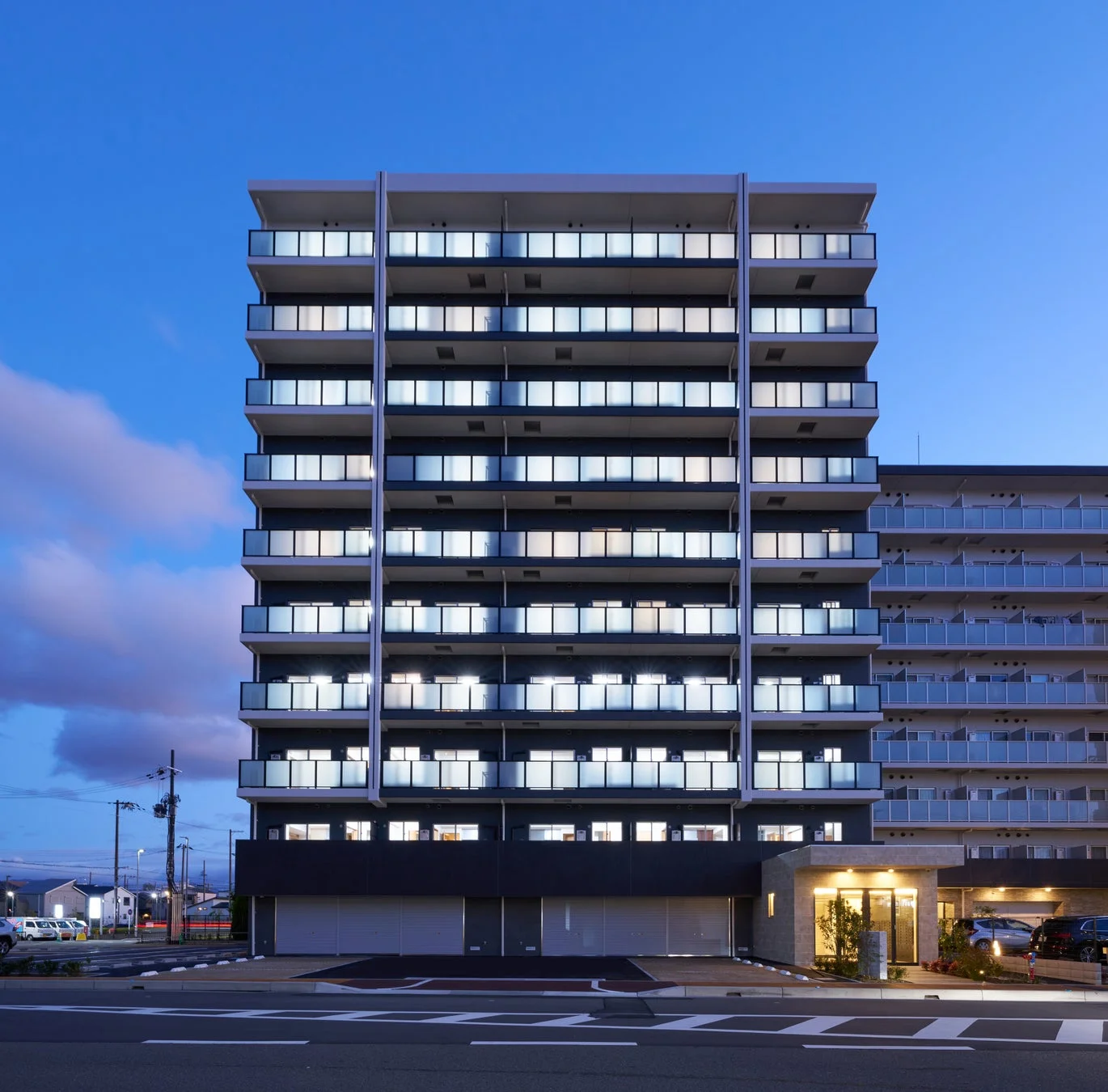 夕暮れ時、多くの窓に明かりが灯るモダンなマンション
