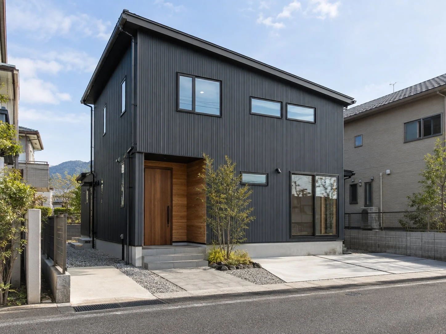 ダークグレーの外壁と木製の玄関ドアが印象的なモダンな二階建て住宅