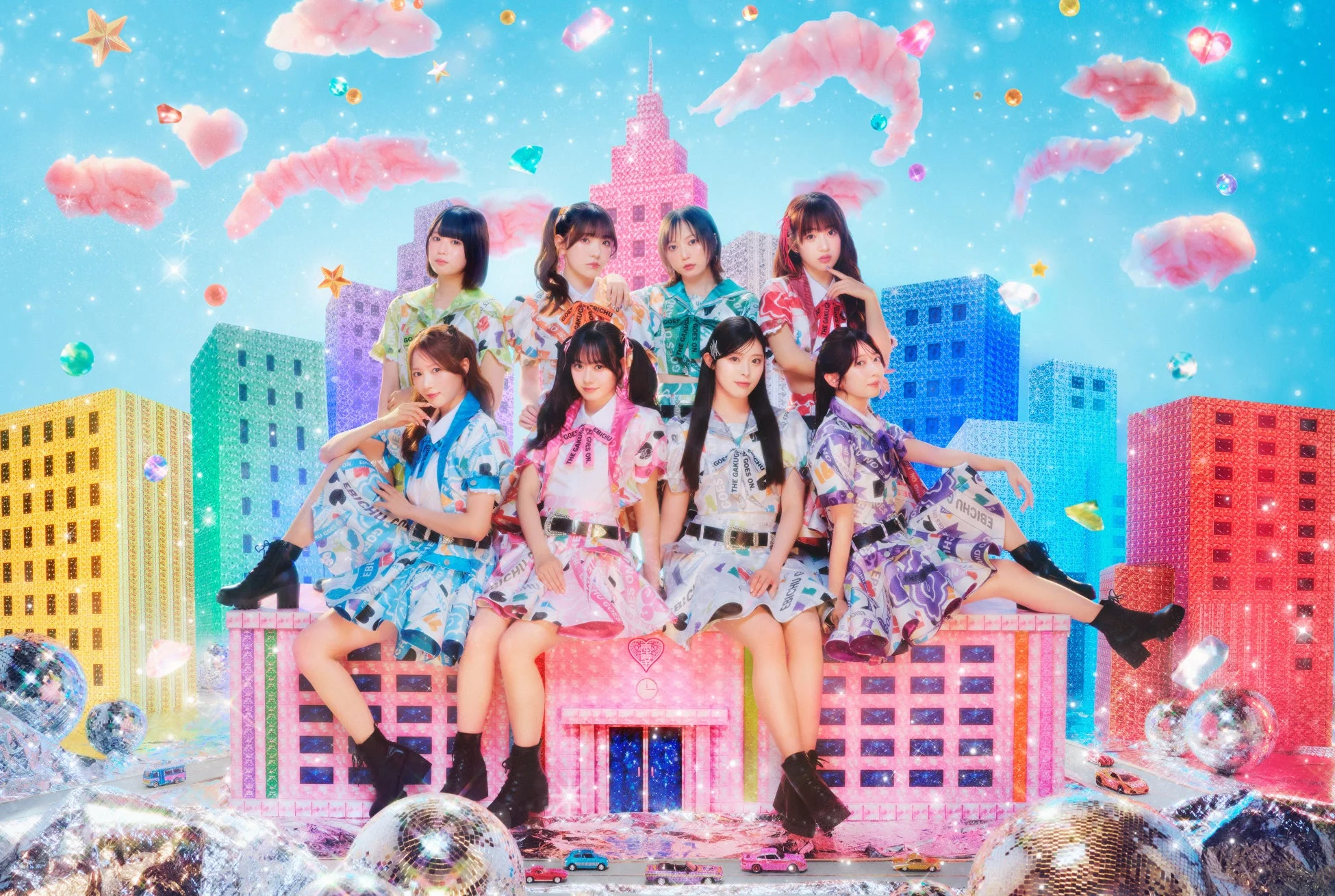 カラフルでキラキラしたファンタジーな都市を背景に、8人組の女性アイドルグループがポーズをとっている